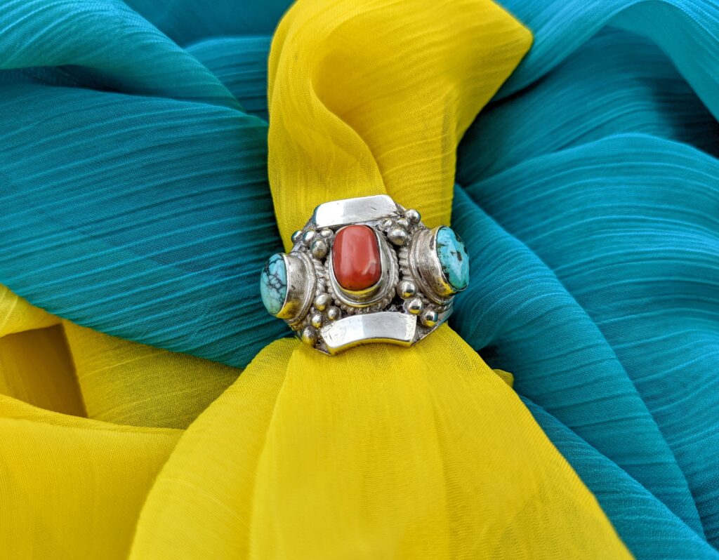 Large vintage turquoise and coral statement ring against and yellow and blue background.