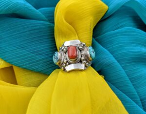 Large vintage turquoise and coral statement ring against and yellow and blue background.