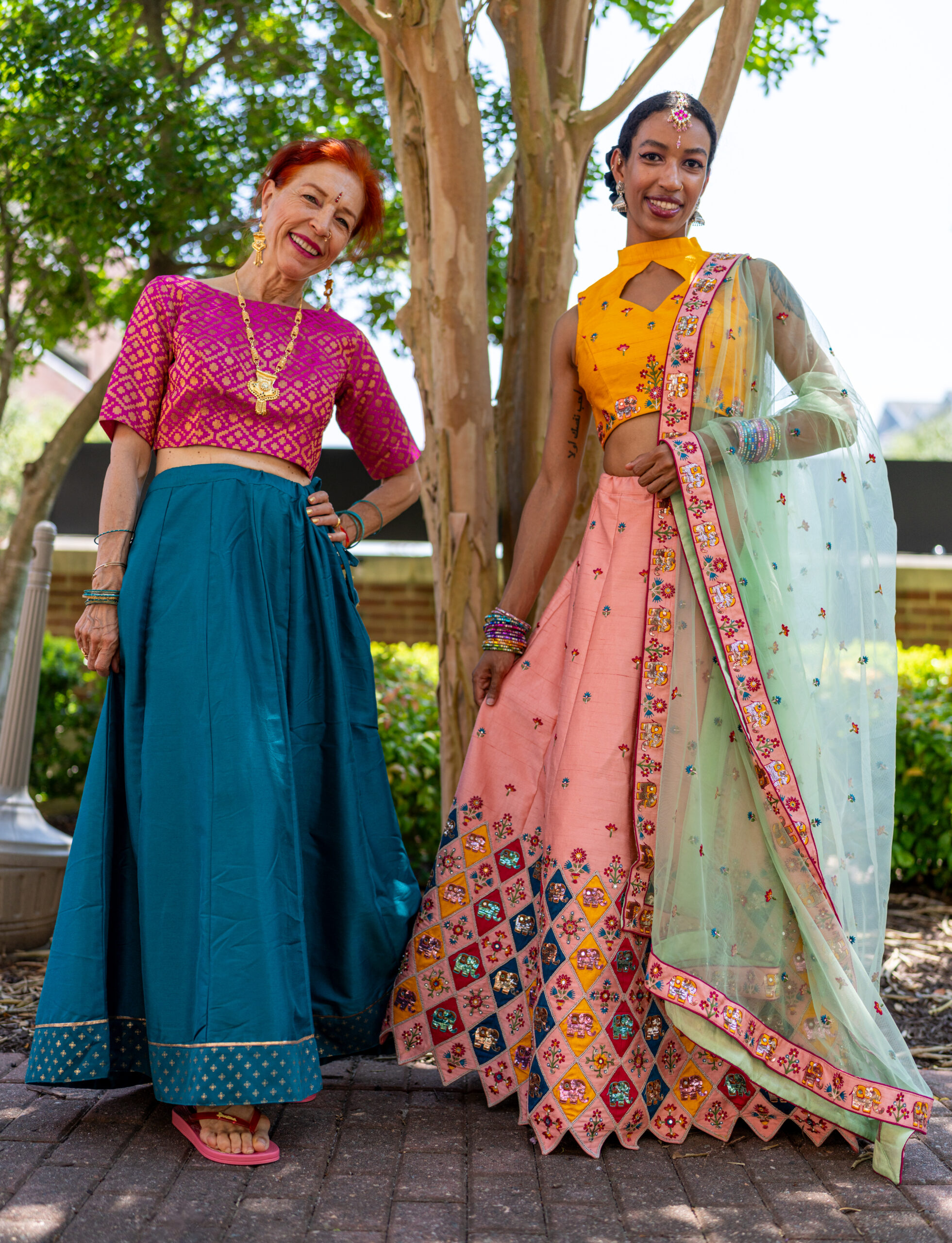 Two dancers posing with elaborate costumes in pink and green in museum garden.