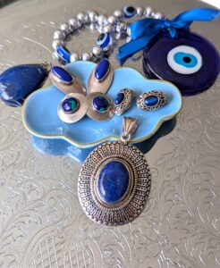 Large lapis pendant with assorted clip earrings in a blue dish, flanked by another lapis pendant and 'the evil eye' glass symbol.